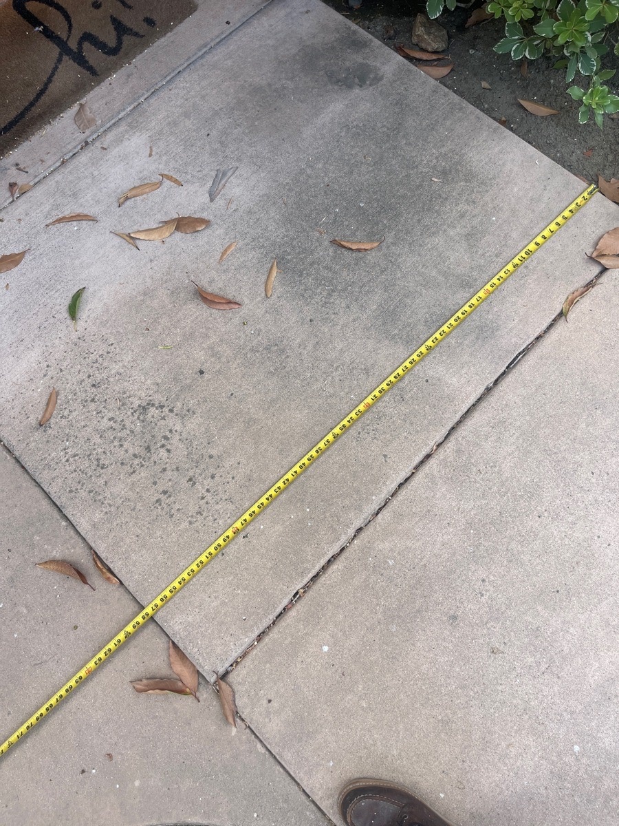Existing cracked and displaced sidewalk panel documented with a tape measure