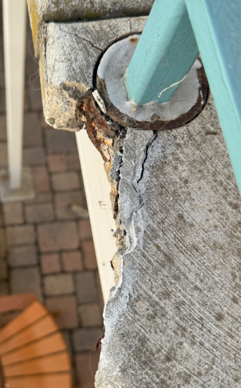 Cracked and missing concrete surrounding a metal handrail post base at a Coronado elevated walkway