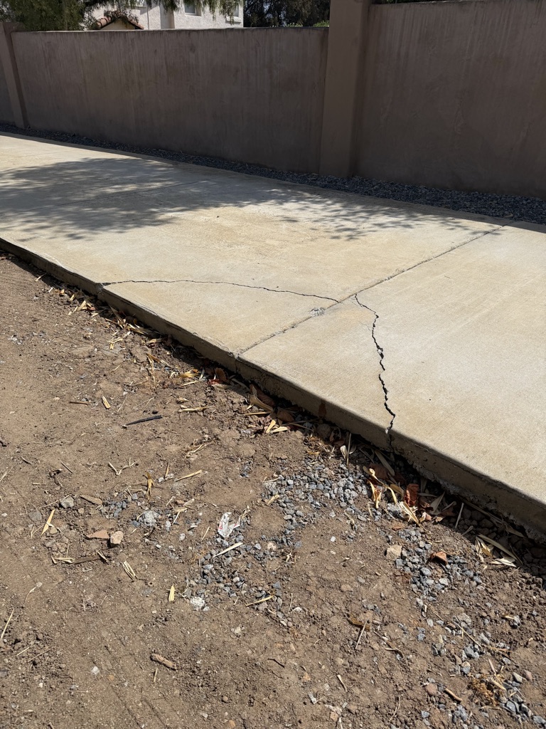 Cracked and chipped driveway edge before a localized concrete repair