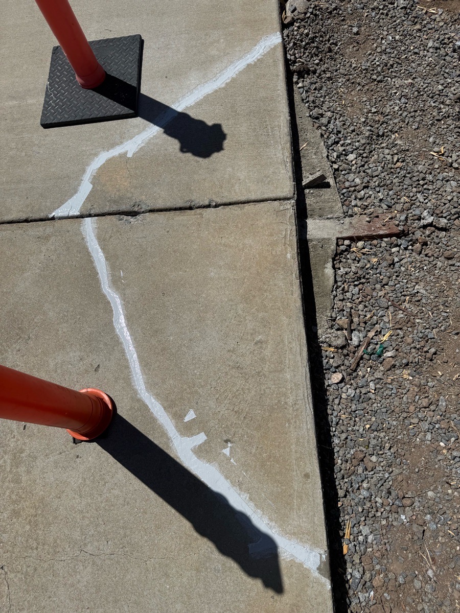 Light-colored localized concrete repair treatment following visible driveway crack lines